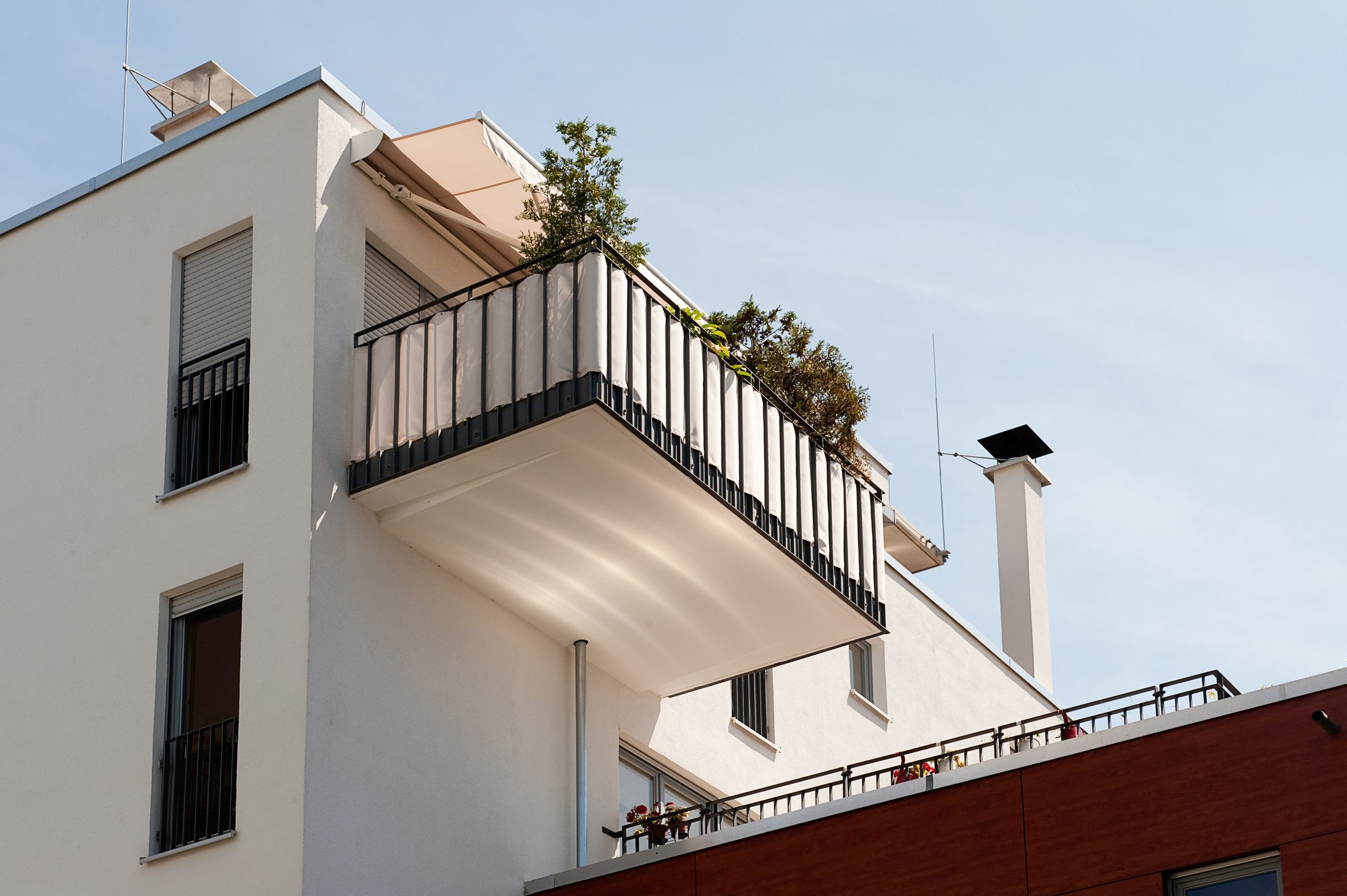 Modernes weißes Wohnhaus mit Dachterrasse und Balkon vor blauem Himmel